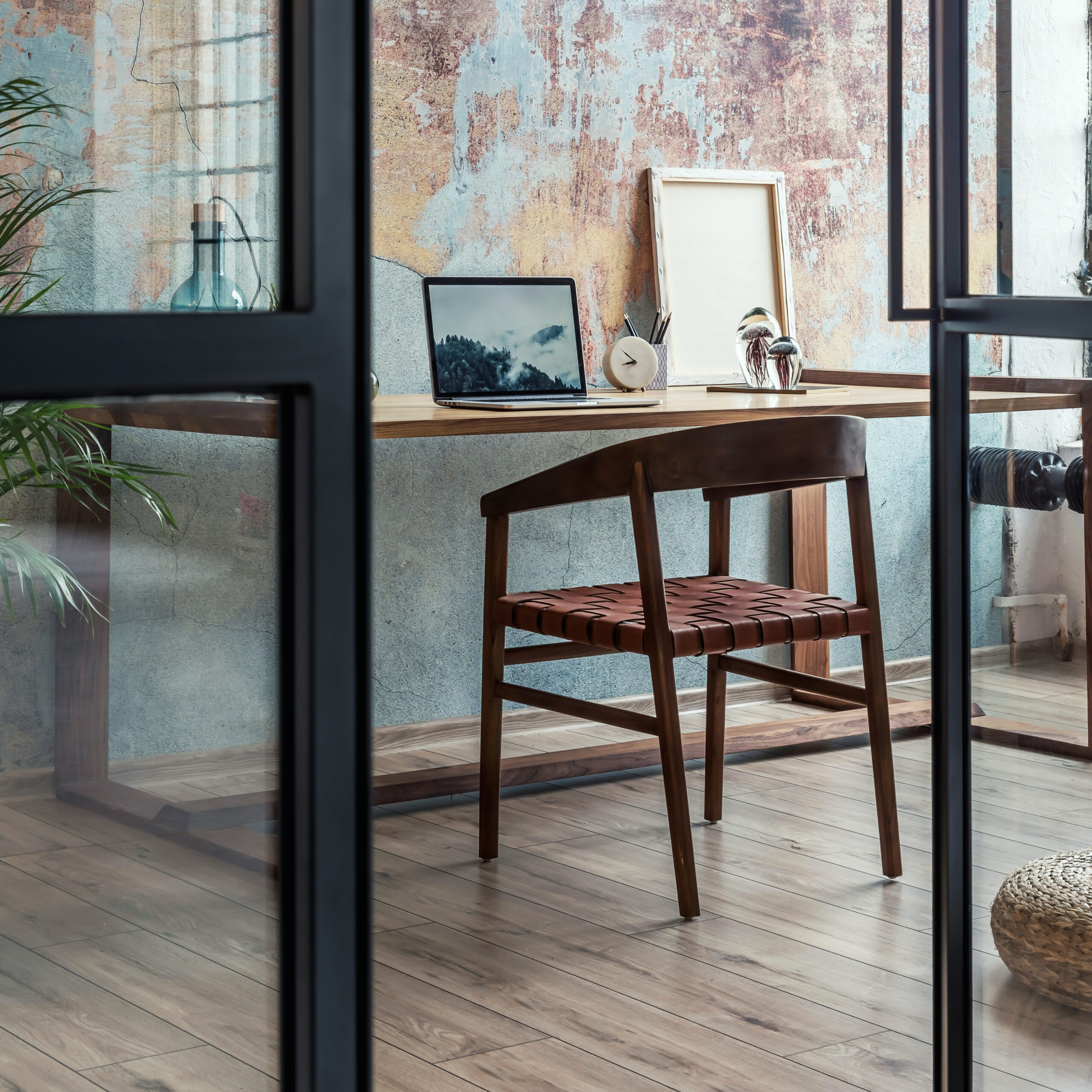 Interior design of stylish office space in loft apartment with wooden desk, chair, office supplies, laptop, plants and elegant accessories. Modern home office decor. Retro wall. Template.